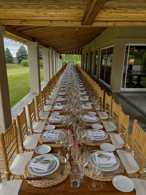 Mesa imperial larga con vajilla blanca, copas y sillas de madera